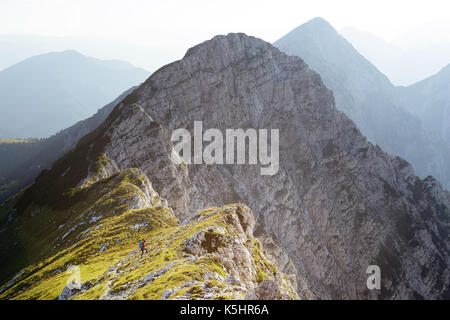 Frau in der roten Jacke, mit Wanderstöcken und Rucksack Wanderungen bis zu einem Aussichtspunkt auf Kladivo, Karawanken, Slowenien. Stockfoto