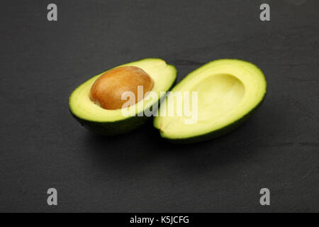 Eine frische reife Avocado Grünschnitt in zwei Hälften mit Grube Stein auf Schiefer Tafel Hintergrund, Detail, Nahaufnahme, erhöht, Ansicht von oben Stockfoto