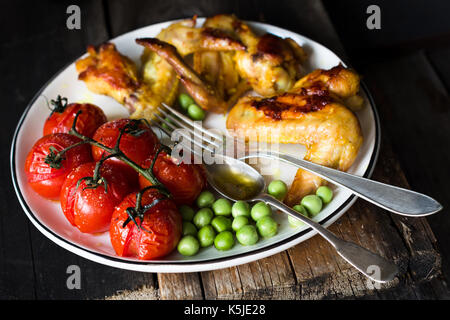 Spicy Chicken Wings, gebratenen Kirschtomaten und sautierten grüne Erbsen auf weiße Platte. Baslanced Mahlzeit. Detailansicht, selektiver Fokus Stockfoto