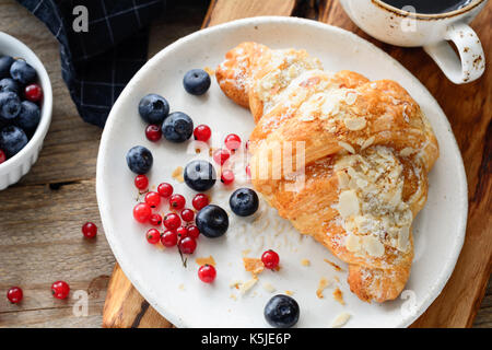 Frische Croissants, Heidelbeeren und roten Johannisbeeren auf weiße Platte. Kontinentales Frühstück. Horizontale Zusammensetzung Stockfoto