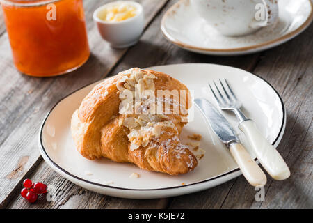 Kontinentales Frühstück Croissant, Marmelade im Glas, Butter und Tasse Kaffee auf hölzernen Tisch. Horizontale Komposition, selektiven Fokus Stockfoto