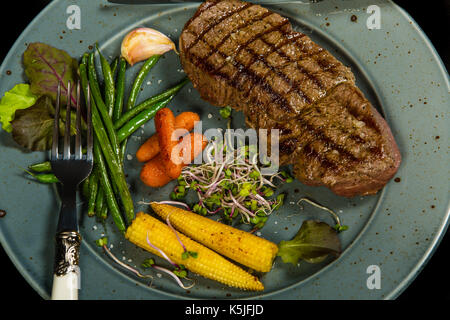 Gegrilltes Rindersteak mit glasierten Gemüse auf dem schwarzen Hintergrund Stockfoto