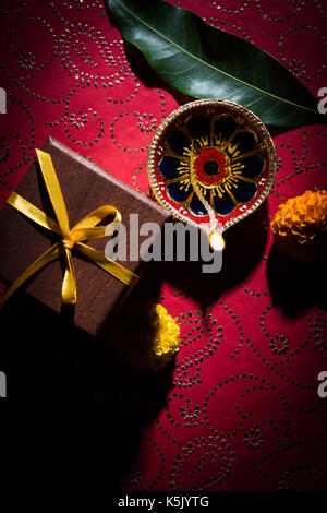 Foto der schönen Diwali diya mit Geschenken und Blumen, über dekorative Hintergrund, stimmungsvolle Beleuchtung und selektiven Fokus Stockfoto