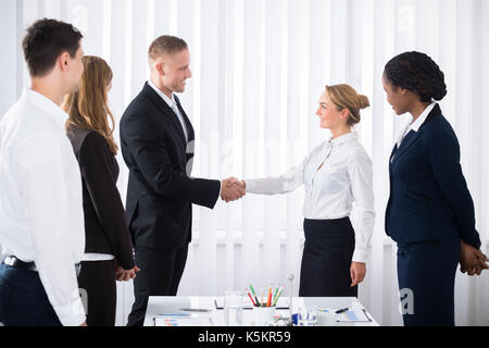 Geschäftsleute, die zwei jungen Geschäftspartner Hände schütteln im Büro Stockfoto