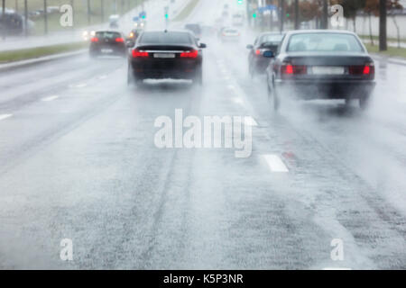 Autos bewegen sich in nassen Straße mit Wasser spritzen von den Rädern. Verschwommene Sicht durch die Windschutzscheibe. Stockfoto