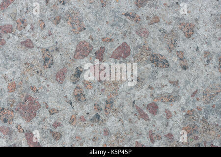 Hintergrund aus Beton mit großen Imprägnierungen aus rotem Granit mit ungleichmäßiger Oberfläche Stockfoto