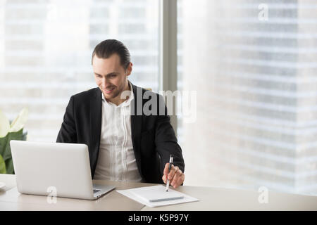 Glücklich lächelnde Geschäftsmann im Büro auf der Suche nach laptop Screen. Stockfoto