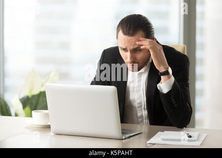 Verärgert verwirrt Geschäftsmann am Laptop Bildschirm am Arbeitsplatz suchen Stockfoto