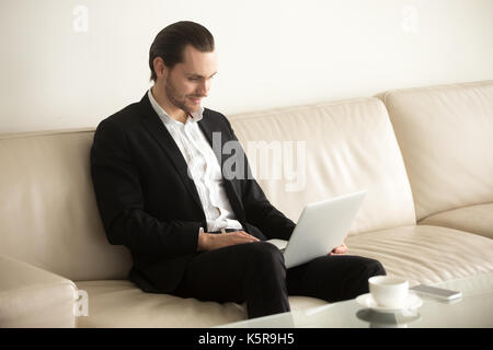 Lächelnd Geschäftsmann auf Laptop fern von zu Hause aus arbeiten. Stockfoto