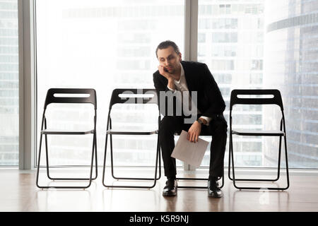 Gelangweilt junger Mann in Anzug im Wartezimmer sitzen. Stockfoto