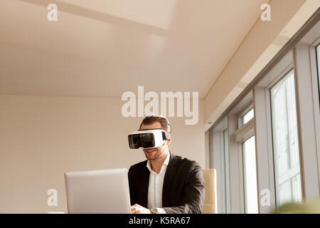 Lächelnd Geschäftsmann im VR-Headset testen Anwendung auf Laptop. Stockfoto
