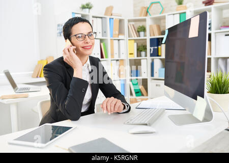 Lächelnd im mittleren Alter Unternehmer sitzen am Schreibtisch während der Durchführung Telefon Verhandlungen mit Business Partner, Interieur des modernen Büro auf backgroun Stockfoto