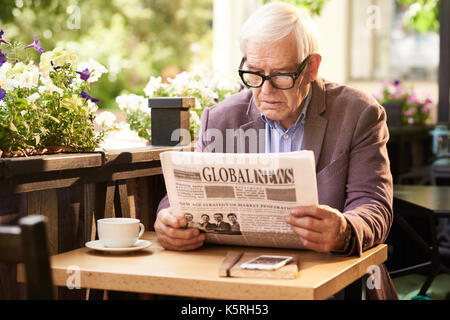 Portrait von älteren Mann lesen Zeitung beim Frühstück im Cafe im Freien Stockfoto