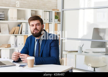 Portrait von erfolgreichen bärtigen Geschäftsmann sie nachdenklich, während am Schreibtisch in modernen Büro arbeiten Stockfoto