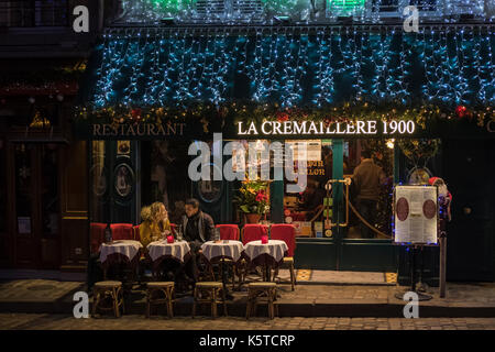 Ein Paar auf der romantischen Terrasse eines Restaurants auf dem Place du Tertre in Montmartre in Paris am Heiligen Abend mit bunten Lichtern. Stockfoto