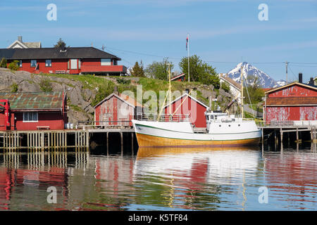 Fischerboot im Hafen mit Rorbu Hütten auf Stelzen in den Norwegischen Dorf vertäut. Ballstad, Vestvågøya, Lofoten, Nordland, Norwegen Stockfoto