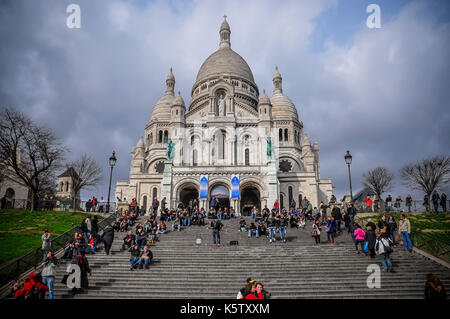 Basilika Sacré-Cœur in Paris Wolken sammeln sich über der Basilika sacré-cœur, während Touristen an einem geschäftigen Tag die ersten Stufen auf- und absteigen. Stockfoto