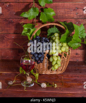 Weintrauben, Rotwein und Rebe auf einem Holztisch Stockfoto