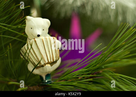 Vintage Glas Weihnachtsbaum Spielzeug: Niedlichen Eisbären mit Akkordeon Nahaufnahme vor dem Hintergrund der grünen Zweige. Unscharfer Hintergrund. Stockfoto