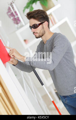 Blinder Mann mit weißem Stick und dunklen Brillen zu Hause Stockfoto