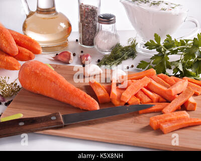 Karotten gehackt auf Stäbchen von Grün, Petersilie, Dill, Knoblauch, Pfeffer umgeben, pflanzliches Öl in eine Flasche mit einem Stopfen, mit Pfeffer und Salz in Gläsern Stockfoto