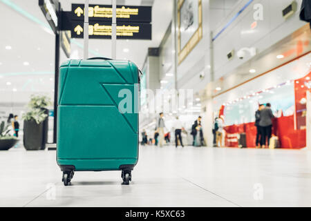 Koffer im Flughafen Abflug Terminal mit reisenden Menschen zu Fuß im Hintergrund, Urlaub, Geschäftsreise, selektiver Fokus auf Koffer Stockfoto