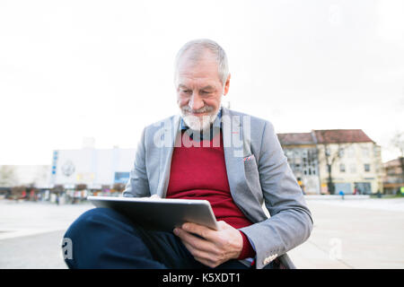 Ältere Mann in der Stadt sitzen auf Bank, arbeitet an tablet Stockfoto