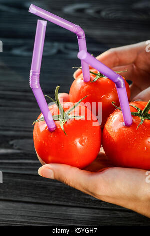 Drei reife rote Tomaten mit Pailletten in Händen auf schwarzem Holz- Hintergrund. Frischer Saft gesundes Essen Konzept. Tomaten wie ein Gefäß mit frischem Saft Stockfoto