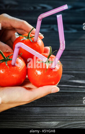 Drei reife rote Tomaten mit Pailletten in Händen auf schwarzem Holz- Hintergrund. Frischer Saft gesundes Essen Konzept. Tomaten wie ein Gefäß mit frischem Saft Stockfoto