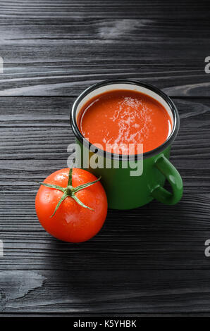 Tomatensaft in Grün Emaille Tasse auf einem schwarzen Holztisch mit frischen Tomaten Ansicht von Oben. Stockfoto