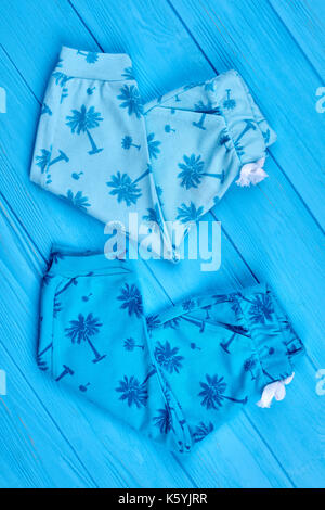 Neuen zusammengeklappten Kinder Sommer Leggings. Baumwolle Palm Tree drucken Baby Hosen auf Blau Holz- Hintergrund, Ansicht von oben. Fashion design Kleinkinder Outfit. Stockfoto