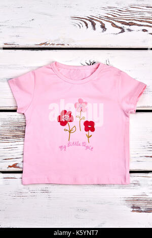 Baby-girl Short Sleeve T-shirt. Kind, Mädchen, rosa Blüten Cartoon-T-Shirt, weiss Holz- Hintergrund. Kinder legere Kleidung. Stockfoto