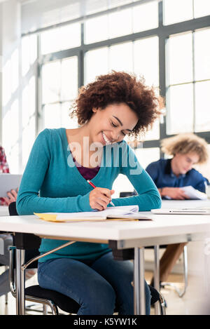 Junge Schülerin mit einem ernsten Gesichtsausdruck Konzentration beim Schreiben einen Aufsatz im Unterricht an einer internationalen Universität Stockfoto