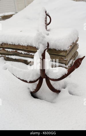 Alten rostigen Haken-lums, Anker mit fünf Zinken links beiseite auf dem schneebedeckten Boden neben einem Stapel der Protokolle im Hof eines White Cottage - touristische Rorbu Stockfoto