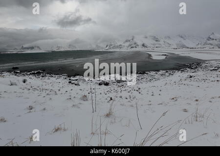 E-SEwards Blick auf verschneite Ytresand Strand - Sandbotnen Bucht - stürmischen Himmel. - Volandstinden-Sautinden Flakstadtinden Nonstinden-Stortinden-Mounts. Ytresand Stockfoto