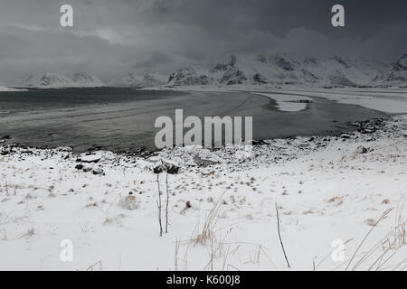 E-SEwards Blick auf verschneite Ytresand Strand - Sandbotnen Bucht - stürmischen Himmel. - Volandstinden-Sautinden Flakstadtinden Nonstinden-Stortinden-Mounts. Ytresand Stockfoto