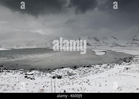 E-SEwards Blick auf verschneite Ytresand Strand - Sandbotnen Bucht - stürmischen Himmel. - Volandstinden-Sautinden Flakstadtinden Nonstinden-Stortinden-Mounts. Ytresand Stockfoto