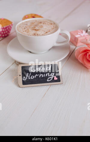 Kaffeebecher mit Kuchen, Rose und Noten guten Morgen auf weißem rustikalen Tisch von oben, leckeres Frühstück Stockfoto