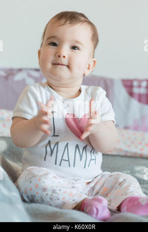 Vertikale erschossen. Das Baby sitzt lächelnd auf dem Bett zu Hause. Stockfoto