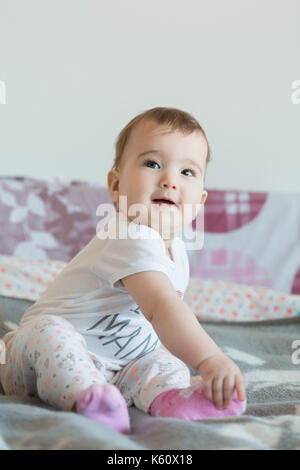 Vertikale erschossen. Das Baby sitzt lächelnd auf dem Bett zu Hause. Stockfoto