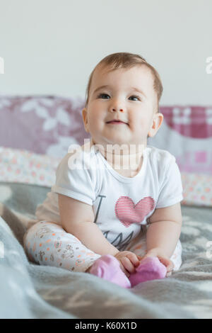 Vertikale erschossen. Das Baby sitzt lächelnd auf dem Bett zu Hause. Stockfoto