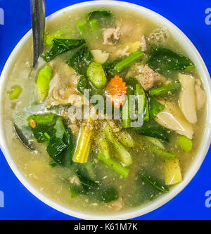 Gebratene flache breite Nudeln mit Schweinefleisch und Kohl in cremiger Sauce Sauce (Thai: Guaitiao Rad Na) in weißen Schale auf der blauen Tabelle Hintergrund. Beliebte asiatische Chinesische Stockfoto