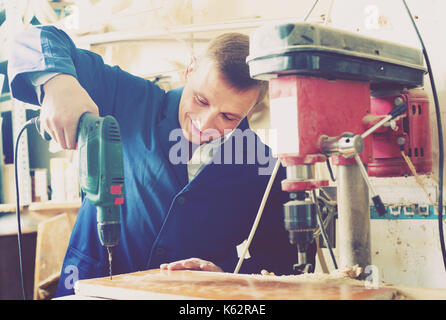 Freundliche Handwerker 40-45 Jahre alt bohren Bohlen über elektrische Schraubendreher in der Werkstatt Stockfoto