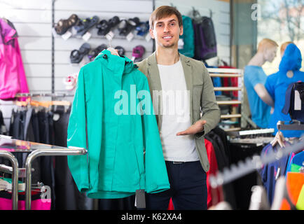 Gewöhnlicher junger Mann Kommissionierung eine Strickjacke im Sport Shop und lächelnd Stockfoto