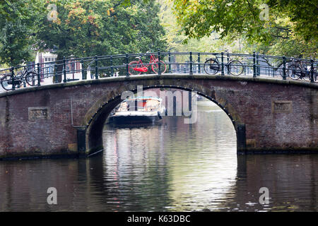 Kanal und ein rotes Fahrrad auf einer Brücke in Amsterdam geparkt Stockfoto