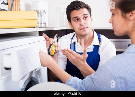 Ernsthafte Veteran und betonte Frau in der Nähe der Waschmaschine in der Küche Stockfoto