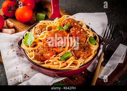 Spaghetti Nudeln mit Hackfleischbällchen, Tomatensauce Basilikum in Rot gusseisernen Pfanne, auf schwarzen Steintisch mit schneidebrett Kopie Raum Stockfoto