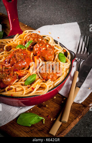 Spaghetti Nudeln mit Hackfleischbällchen, Tomatensauce Basilikum in Rot gusseisernen Pfanne, auf schwarzen Steintisch mit schneidebrett Kopie Raum Stockfoto