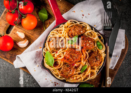 Spaghetti Nudeln mit Hackfleischbällchen, Tomatensauce Basilikum in Rot gusseisernen Pfanne, auf schwarzen Steintisch mit schneidebrett Kopie Raum, Ansicht von oben Stockfoto