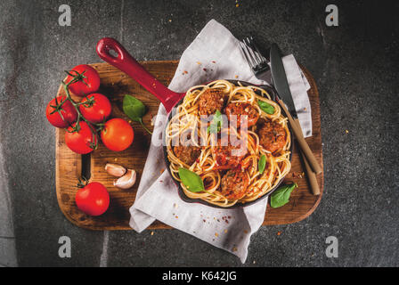 Spaghetti Nudeln mit Hackfleischbällchen, Tomatensauce Basilikum in Rot gusseisernen Pfanne, auf schwarzen Steintisch mit schneidebrett Kopie Raum, Ansicht von oben Stockfoto